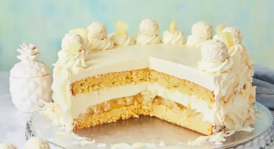 Eine köstliche Piña Colada Torte mit Kokosraspeln und Ananasstücken, verziert mit Sahnetuffs und Pralinen.