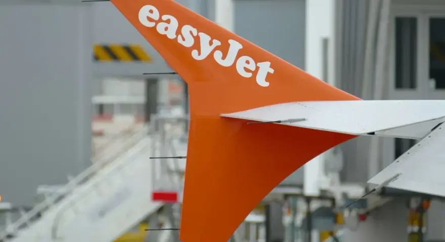 Pomarańczowy statecznik pionowy samolotu easyJet z białym logo, gotowy do przyjęcia bagażu pasażerów.