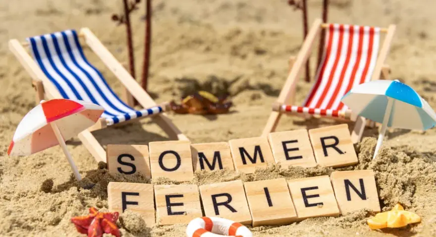 Strandkörbchen, Palmen und die Worte "Sommerferien" im Sand. Perfekt für die Sommerferien in Brandenburg!