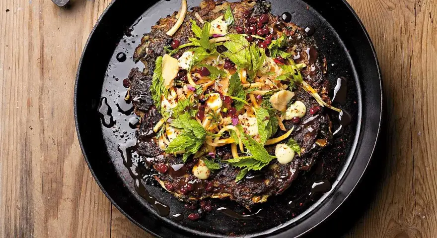 En mörk, krispig pannkaka med kirskål, toppad med färska örter, granatäppelkärnor och en krämig dressing. Ett spännande kirskål recept!