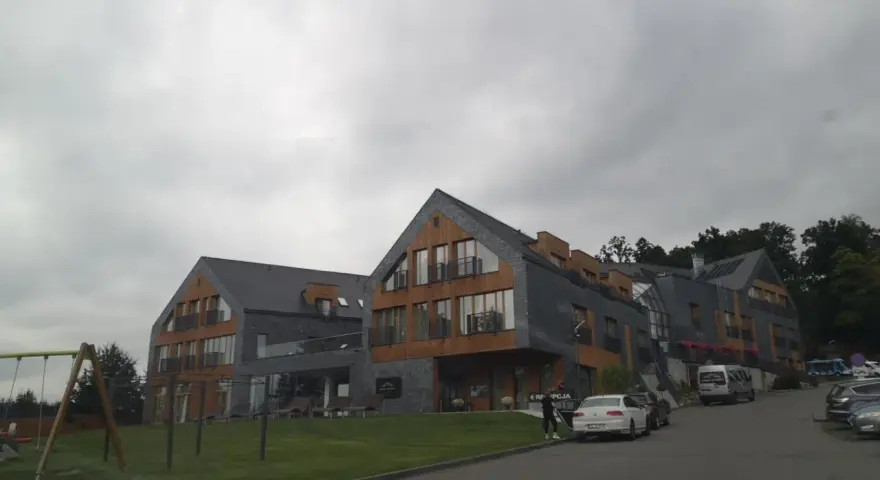 Nowoczesny hotel z drewnianymi elementami i kamienną elewacją. Na trawniku plac zabaw. Wiele pozytywnych osada-sniezka opinie potwierdza jego urok.