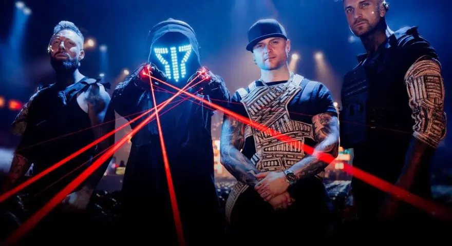Czterech mężczyzn w futurystycznych strojach, z maską LED i czerwonymi laserami na scenie.
