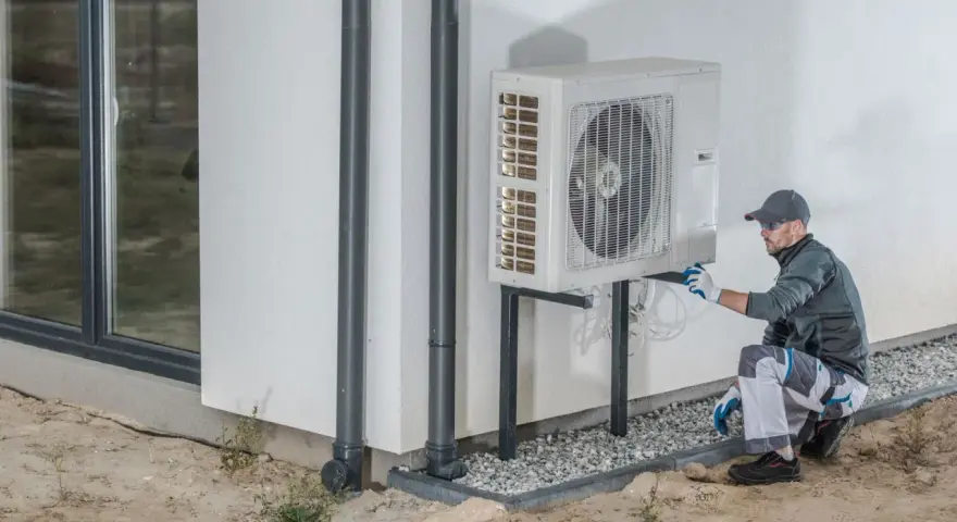 Technik wykonuje protokół uruchomienia pompy ciepła, sprawdzając instalację przy ścianie budynku.