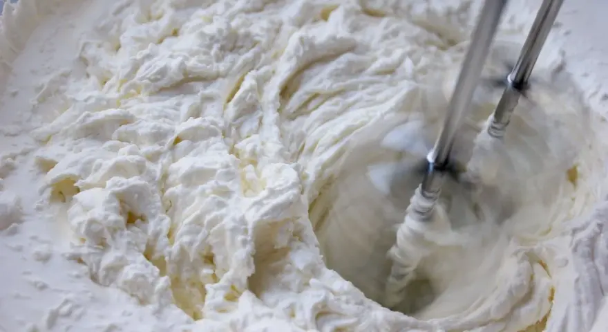 Batidora eléctrica batiendo crema blanca y espesa en un bol.