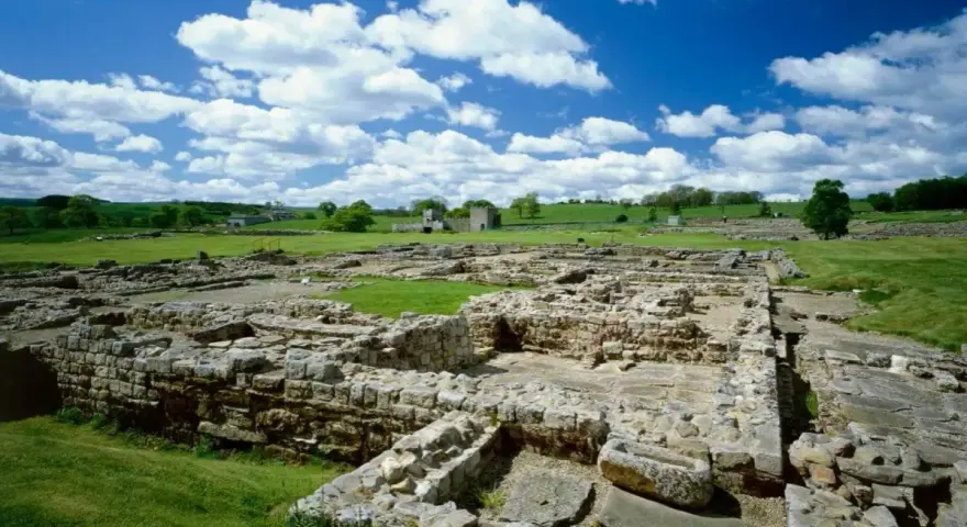 Extensive roman ruin spread across a green field under a blue sky with fluffy clouds.