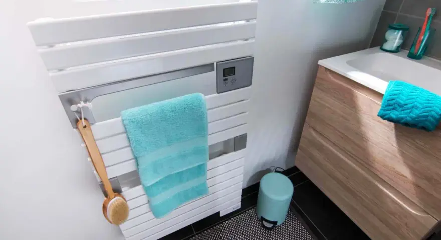 Un sèche-serviettes blanc moderne, avec une serviette turquoise et une brosse de bain en bois. La hauteur du sèche-serviette est idéale pour un accès facile.