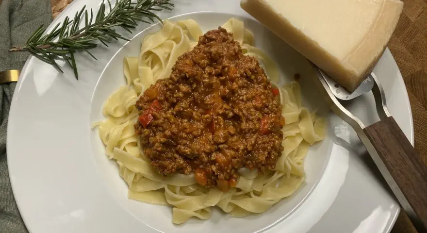 Ein Teller Tagliatelle mit herzhafter Bolognese, garniert mit Rosmarin und Parmesan.