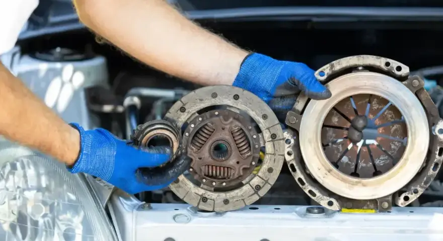 Mechanik w niebieskich rękawiczkach pokazuje zużyte części sprzęgła, które mogą być przyczyną ślizgającego się sprzęgła objawy.