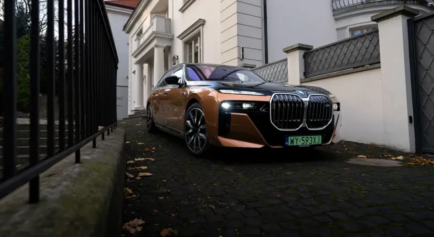 Eleganckie BMW i7 w miedzianym kolorze, zaparkowane przed willą. Ten luksusowy samochód elektryczny oferuje imponujący zasięg, pozwalając na długie podróże.