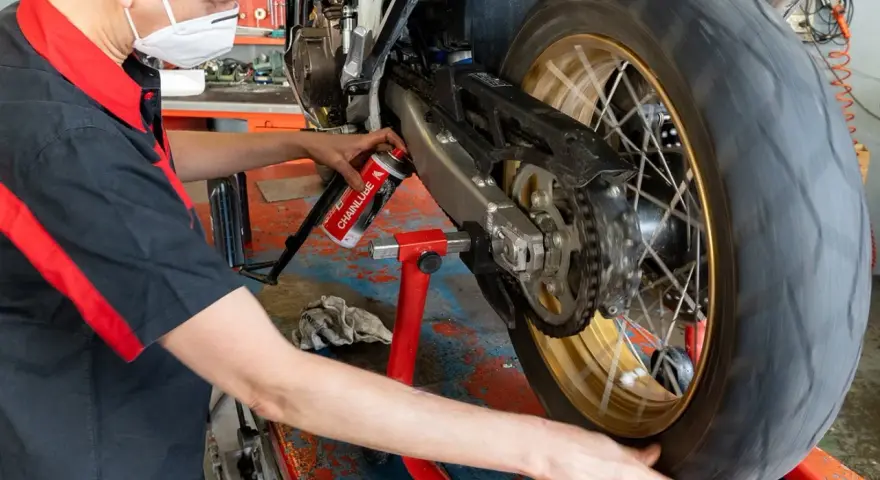 Meccanico lubrifica la catena di una moto. La pulizia catena moto ogni quanti km è fondamentale per la sua durata.