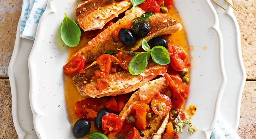 Deliziosa gallinella di mare in umido con pomodorini, olive nere e capperi, guarnita con basilico fresco.
