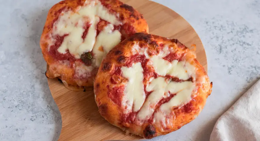 Due pizzette fatte in casa, con pomodoro e mozzarella filante, su un tagliere di legno.