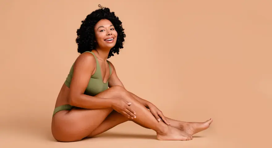 Femme souriante en sous-vêtements verts, caressant sa jambe. Elle partage ses secrets pour comment avoir des pieds doux.