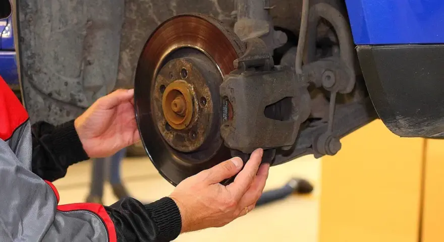 Mechanik sprawdza klocki hamulcowe, dotykając zacisku i tarczy hamulcowej.