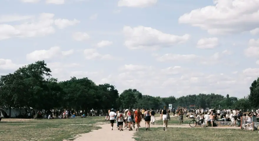 Menschen spazieren an einem sonnigen Pfingstmontag in Berlin durch eine grüne Parklandschaft.