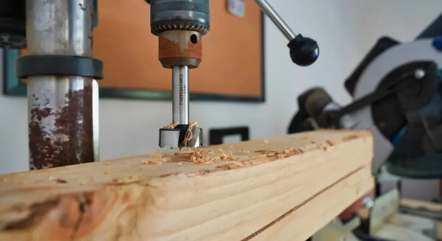 Trapano a colonna che fora un pezzo di legno, creando trucioli. Un esempio pratico di come avvitare una vite nel legno, o meglio, preparare il foro.