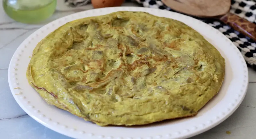 Frittata di carciofi dorata e soffice su un piatto bianco, pronta per essere gustata.