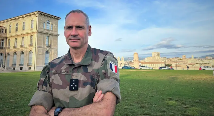 Un officier français, P. Schill, pose devant un bâtiment historique. Comment retrouver un officier ? Il suffit de regarder son uniforme et son insigne.