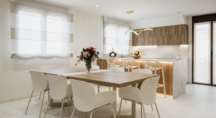 Elegantes cocinas abiertas al salón con barra, mesa de comedor y sillas blancas.