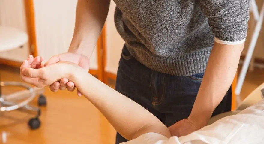 Fizjoterapeuta delikatnie masuje nadgarstek pacjenta, co jest kluczowe, kiedy zacząć rehabilitacja po operacji cieśni nadgarstka.