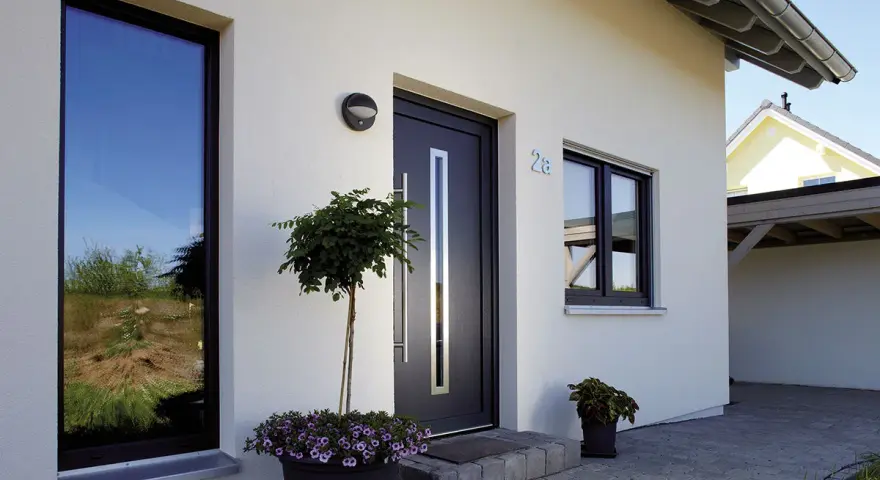Piante e fiori per abbellire ingresso esterno casa. Porta moderna con maniglia lunga, finestre e numero civico 28.