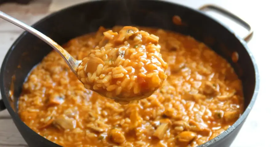 Cuchara llena de cremoso arroz con pollo de la abuela, humeante y con trozos de pollo y champiñones.
