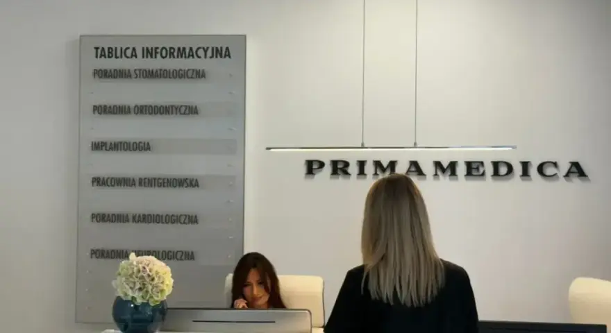 Recepcja gabinetu stomatologicznego Primamedica z tablicą informacyjną i pracownicą.