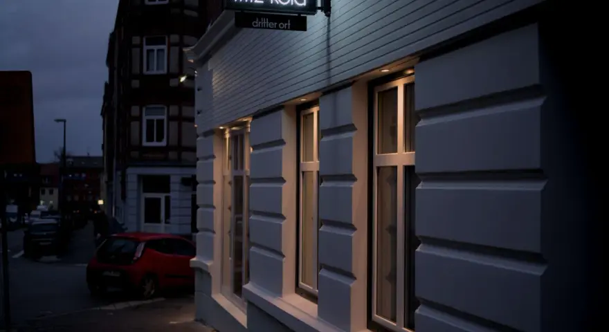 Neon-Schild "fritz-kola" über dem Eingang "dritter ort kiel". Ein rotes Auto parkt auf der Straße.