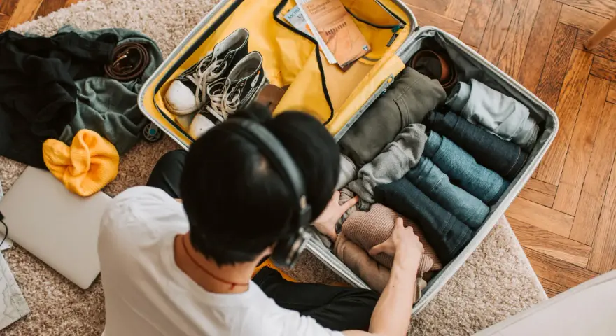 Preparazione per il mare: una valigia piena di vestiti piegati, scarpe, una felpa gialla e un laptop. Ecco cosa portare in vacanza al mare!