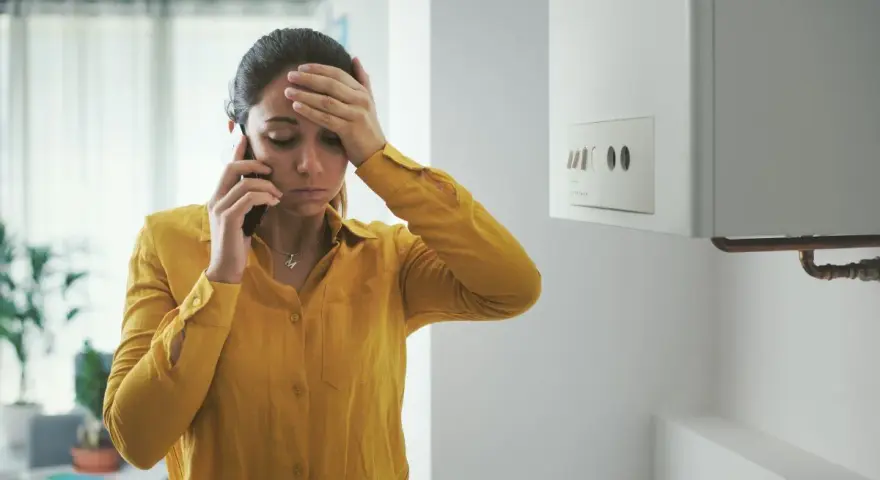 Donna preoccupata al telefono vicino allo scaldabagno, cerca consigli su come evitare il calcare.