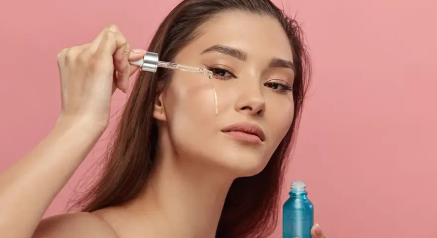Kobieta aplikuje serum z retinyl palmitate na skórę pod okiem. Błękitna buteleczka kosmetyku w dłoni.