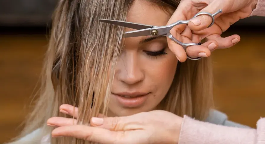 Manos cortando el flequillo de una mujer. Un momento perfecto para saber cuando es mejor cortarse el pelo y renovar tu look.