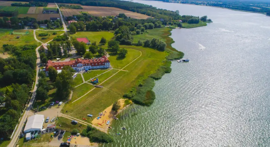 Widok z lotu ptaka na **zalew domaniow** z hotelem, plażą, kajakami i łodziami.