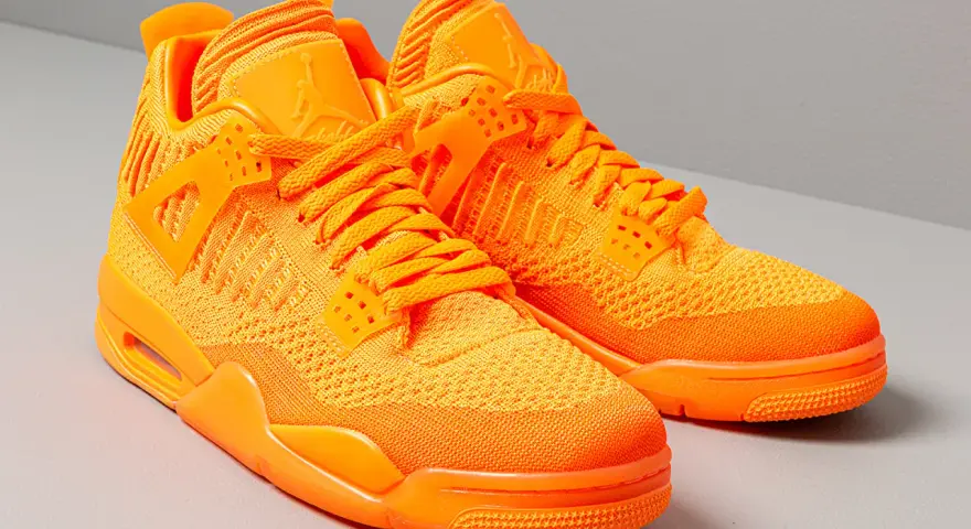 Un paio di scarpe Jordan 4 arancioni brillanti, con tomaia in maglia e dettagli iconici.