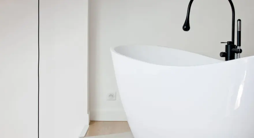 Baignoire îlot blanche au design moderne, avec robinetterie noire. Sa forme suggère une largeur baignoire standard, idéale pour un confort optimal.