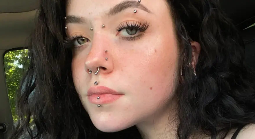 Dziewczyna z licznymi kolczykami: w nosie, ustach, brodzie i na czole. Wyróżnia się anti eyebrow piercing.
