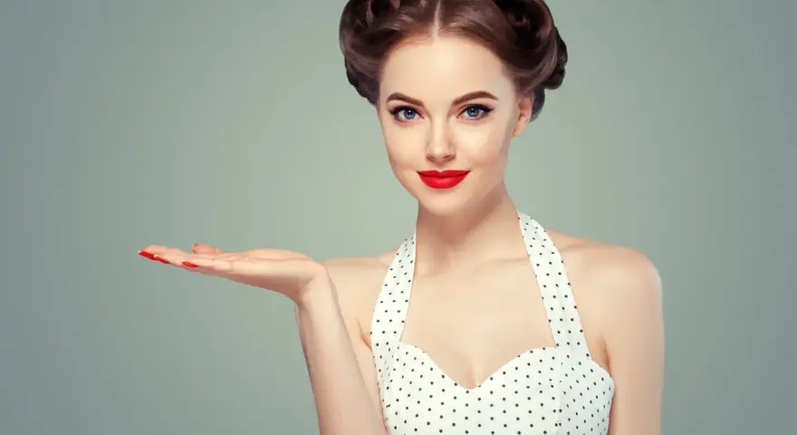 Kobieta w stylu pin-up z burzą loków i czerwoną szminką prezentuje dłoń.