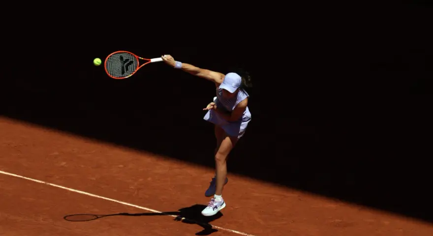 Tenisistka w skoku serwuje piłkę na korcie ziemnym podczas Roland Garros.