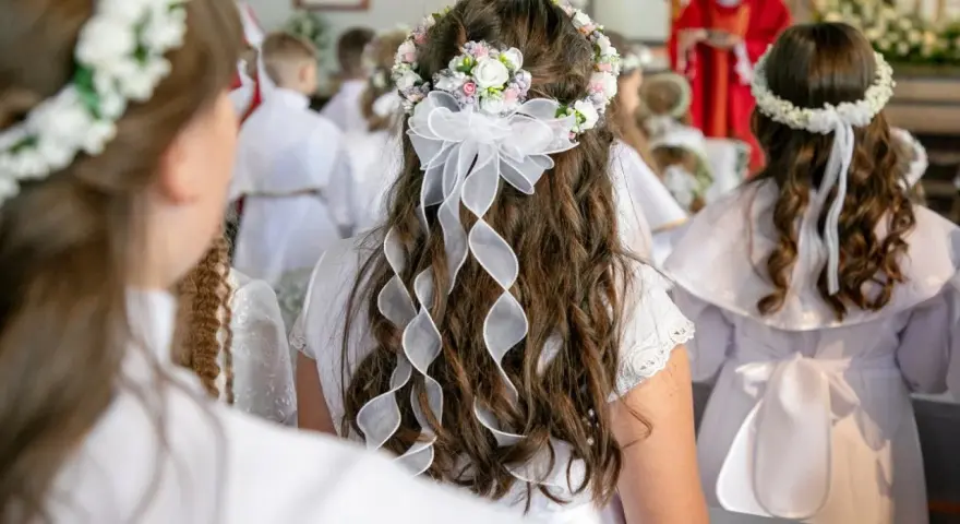 Dzieci w białych strojach, z wiankami na głowach, czekają na swoją pierwszą komunię. Wzruszający moment w kościele.
