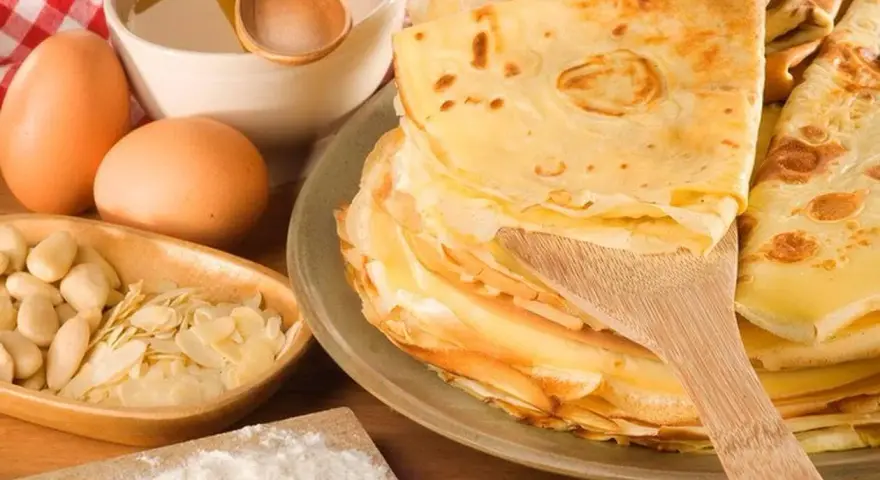 Pile de crêpes dorées, ingrédients pour leur origine : œufs, amandes, farine, miel. Un délice sucré.