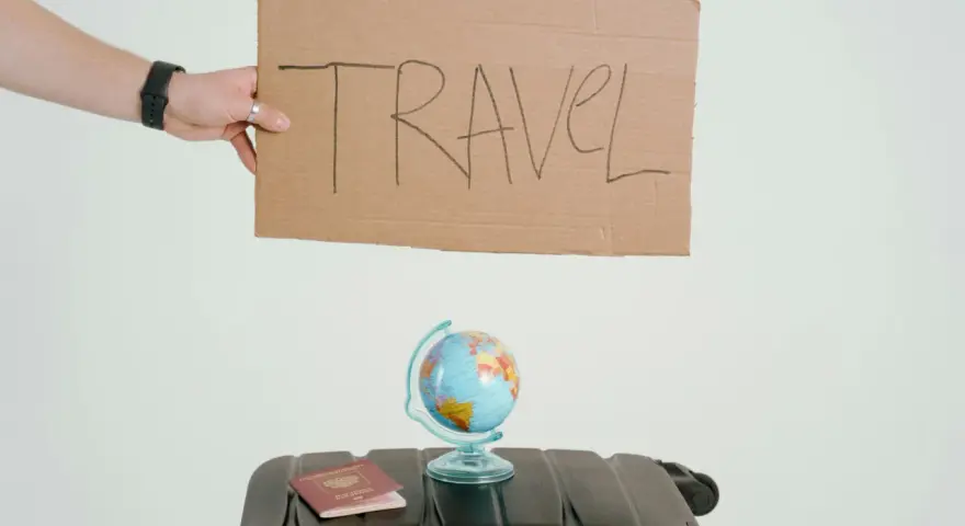 Ręka trzyma tabliczkę z napisem TRAVEL. Obok walizka, globus i paszport. Czy to zapowiedź kolejnych pozytywnych emka travel opinie?