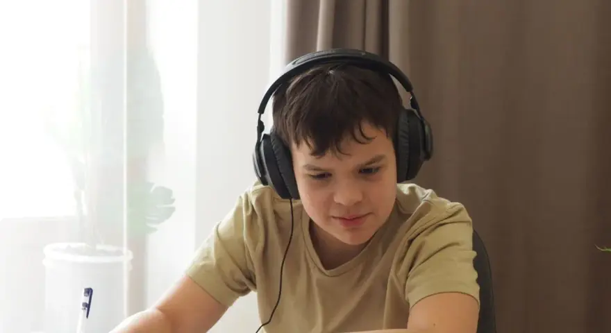 Chłopiec w słuchawkach uczy się zdalnie, notując. Dopełnienie odpowiada na pytania: kogo? czego? komu? czemu? kogo? co? czym? kim? o kim? o czym?