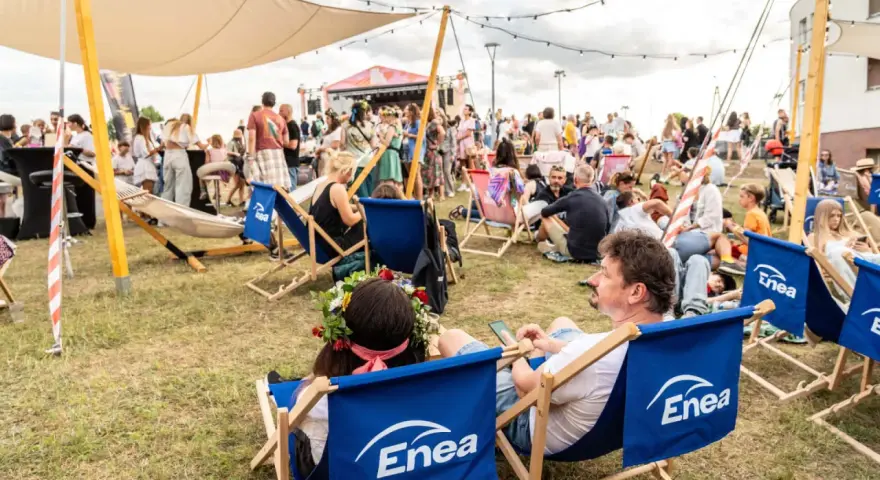 Ludzie odpoczywają na leżakach z logo Enea podczas festiwalu. W tle scena i tłum.