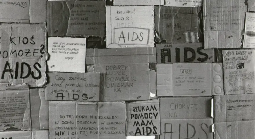 Złe ojciec, zniszczony przez AIDS, błaga o pomoc. Kartony z napisami "AIDS", "SOS", "Ratunku!" i prośbami o wsparcie.