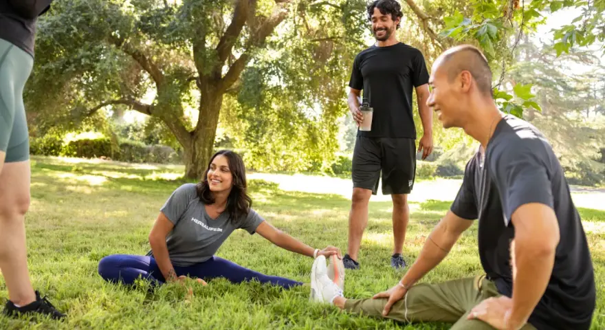 Un grupo de amigos hace estiramientos en un parque. Uno de ellos, que bebe un batido, bromea diciendo que "la creatina engorda", pero todos se ríen y siguen entrenando.