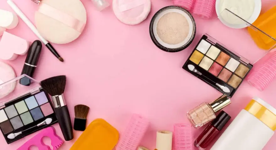 Tanti prodotti per il make-up, tra cui ombretti, rossetti e pennelli, disposti su sfondo rosa. Attenzione, gli ombretti scadono!