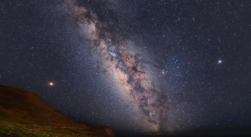 Paisaje nocturno en una reserva starlight, con la Vía Láctea cruzando el cielo estrellado sobre una colina y vegetación.