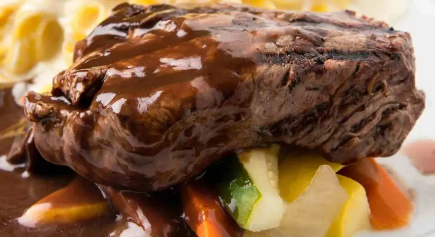 Succulento brasato di manzo nappato con salsa scura, servito su verdure miste e accompagnato da pasta.