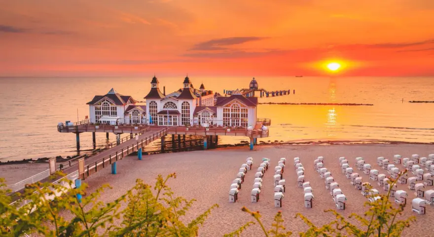 Zachód słońca nad molo w Sellin, na Rugii, największej wyspie Niemiec. Puste kosze plażowe czekają na gości.