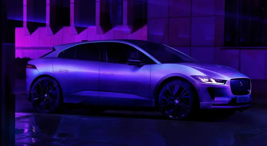 Jaguar I-Pace w fioletowym świetle, zaparkowany na mokrej nawierzchni.